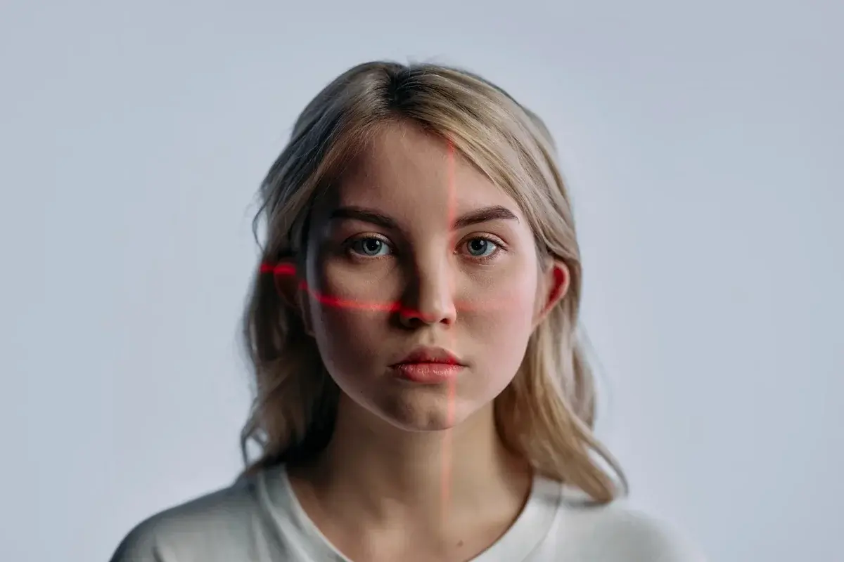 Close-up portrait of a young woman with red facial recognition laser lines across her face.