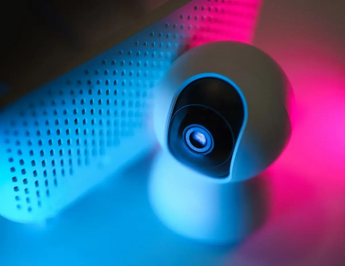 Close-up of a surveillance camera lit by blue and pink neon light.