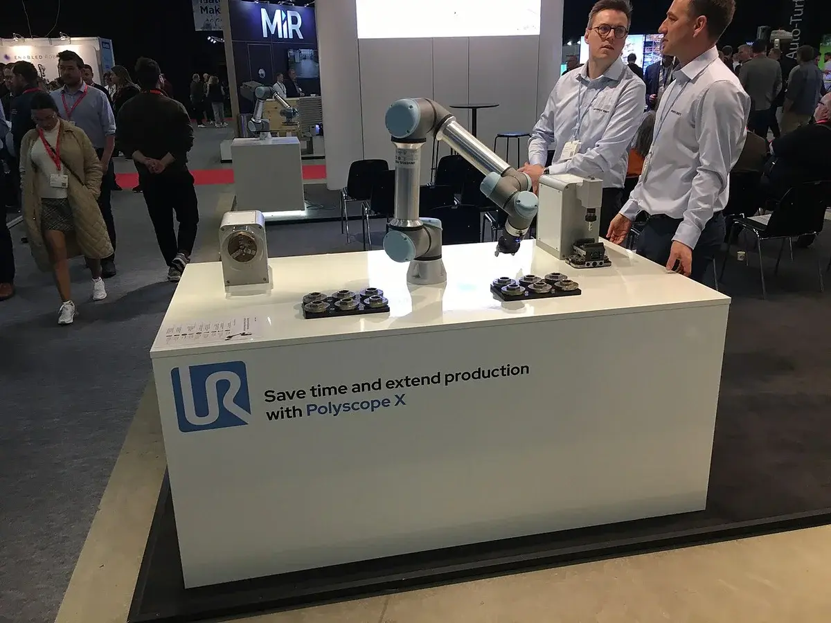 A robot arm on display at a trade show booth with two men nearby.