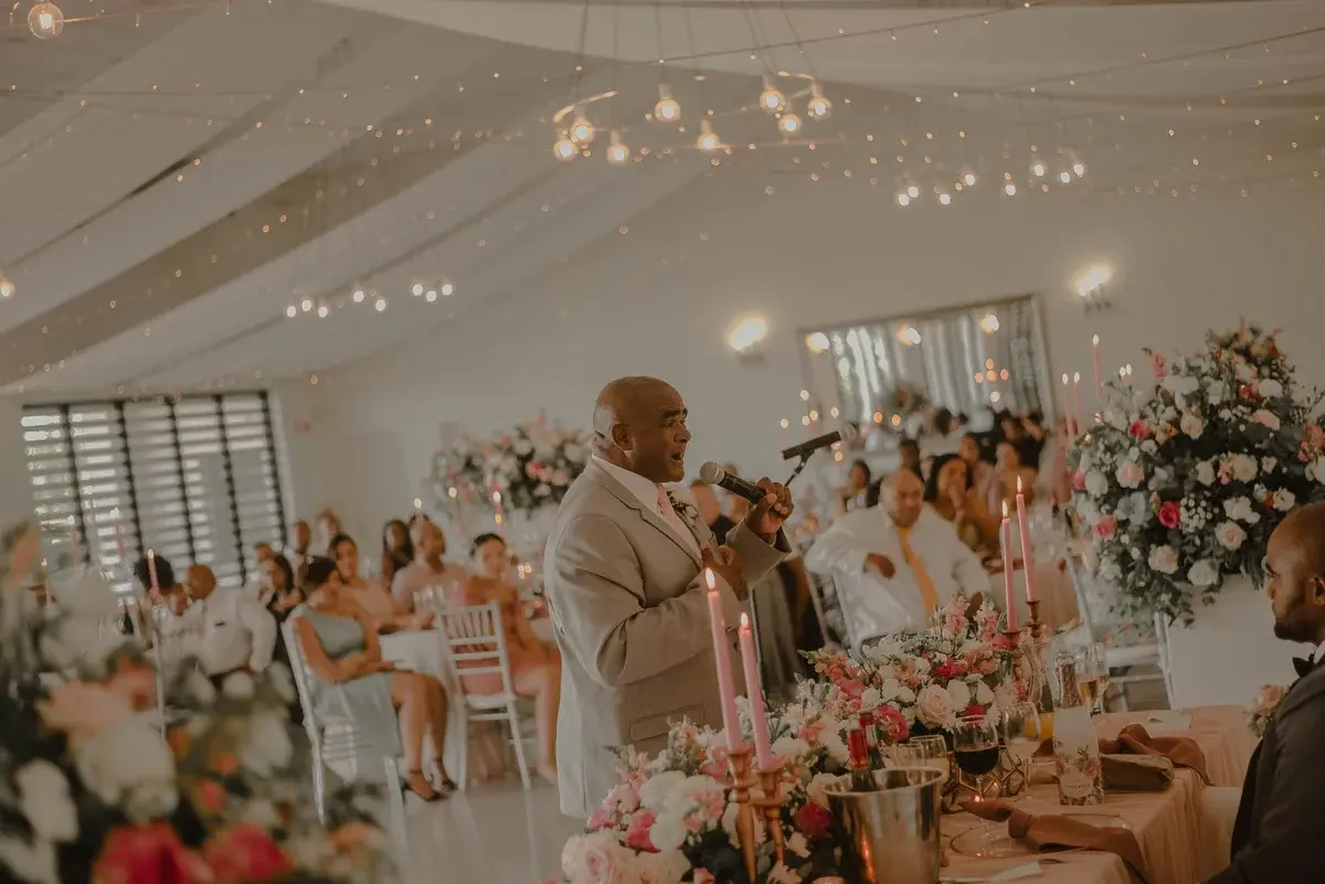 A man speaks into a microphone at a decorated wedding reception.