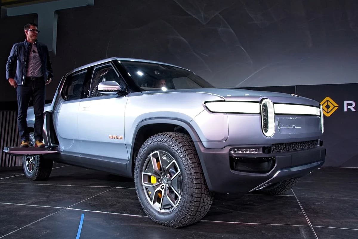 RJ Scaringe stands next to a Rivian R1T pickup truck on stage.