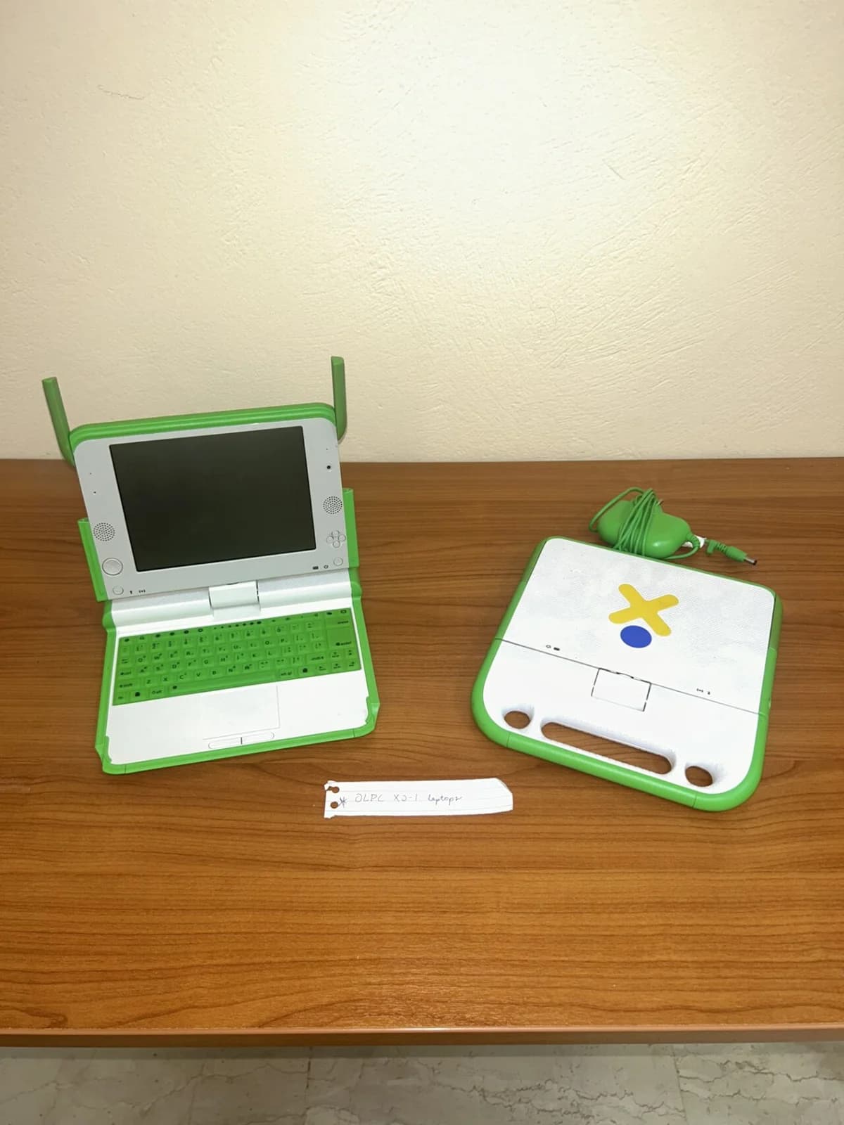 An OLPC XO-1 laptop on a table with its charger and cover piece.