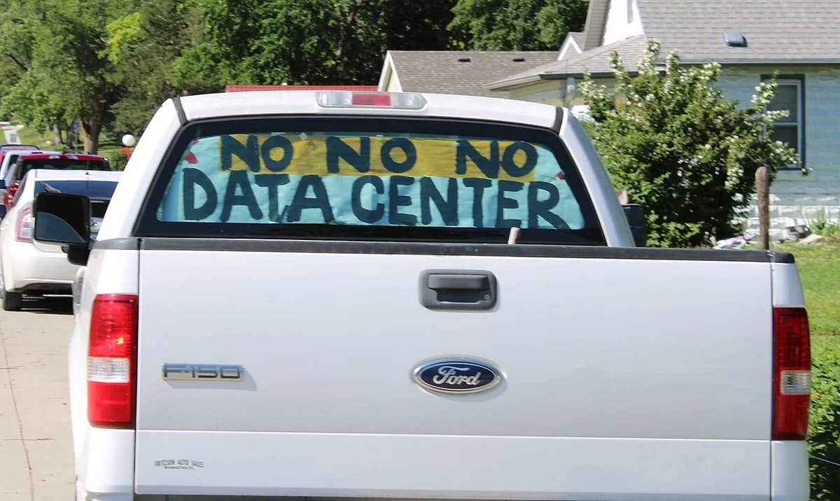 A pickup truck with a rear-window sign reading 'NO NO NO DATA CENTER' parked in a neighborhood.