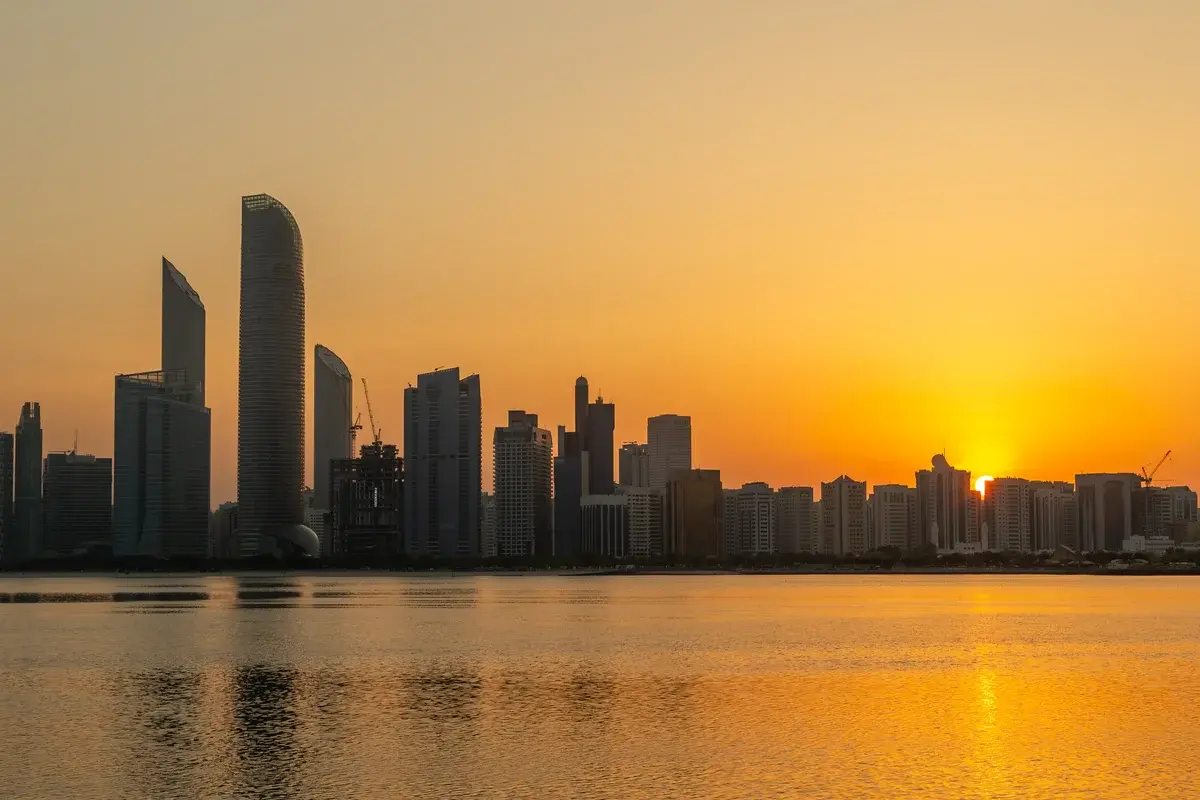 Sunrise over the Abu Dhabi skyline with golden light reflecting on the water.