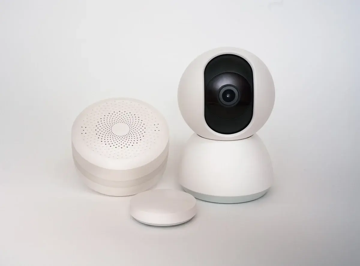 White smart home security camera and sensors on a plain background.