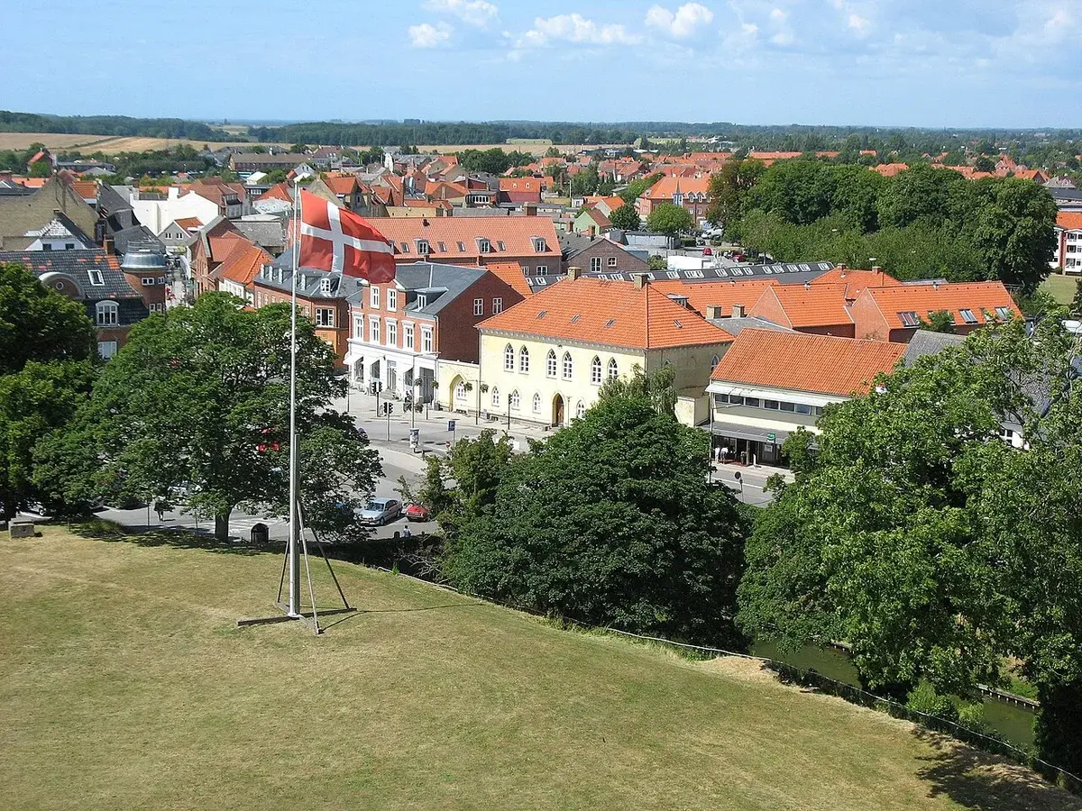 Elevated view over a Danish town with red-roofed buildings and a Danish flag.