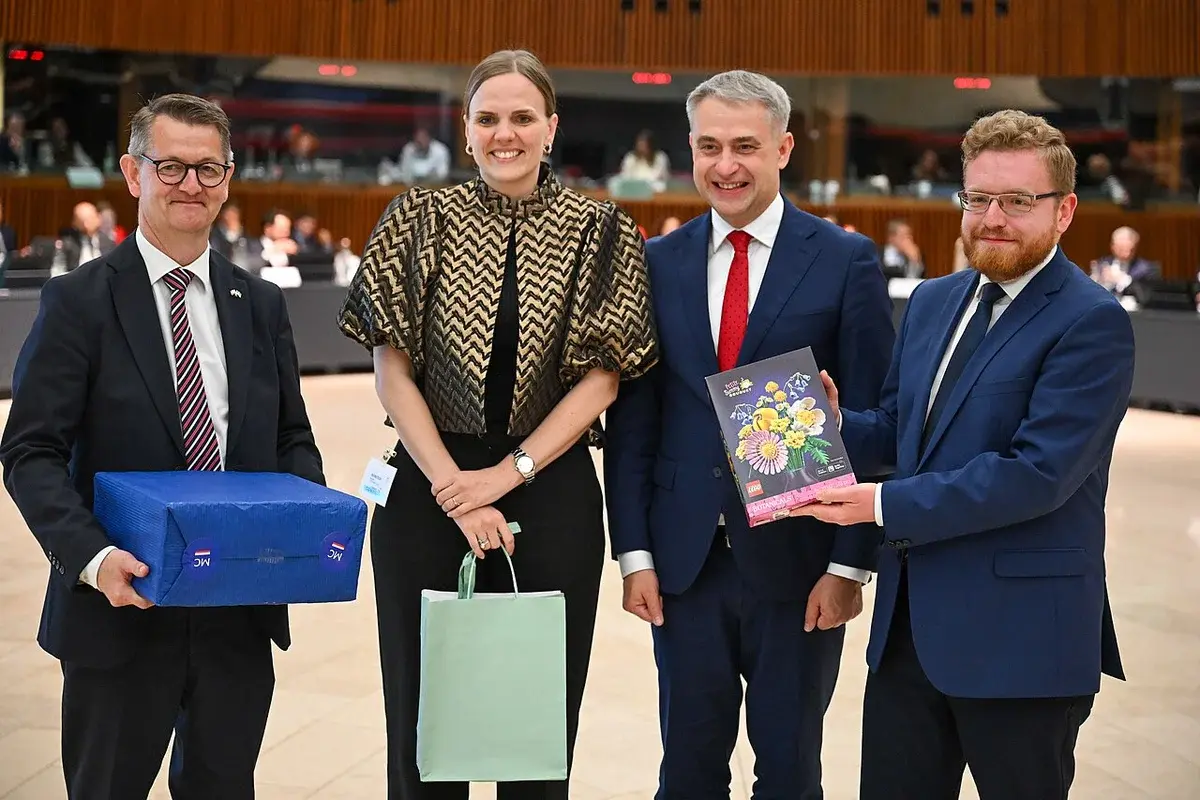 Four officials posing together at a council meeting, holding gifts.