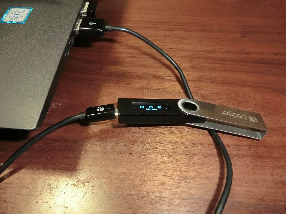 A Ledger Nano S hardware wallet connected to a laptop by USB cable.