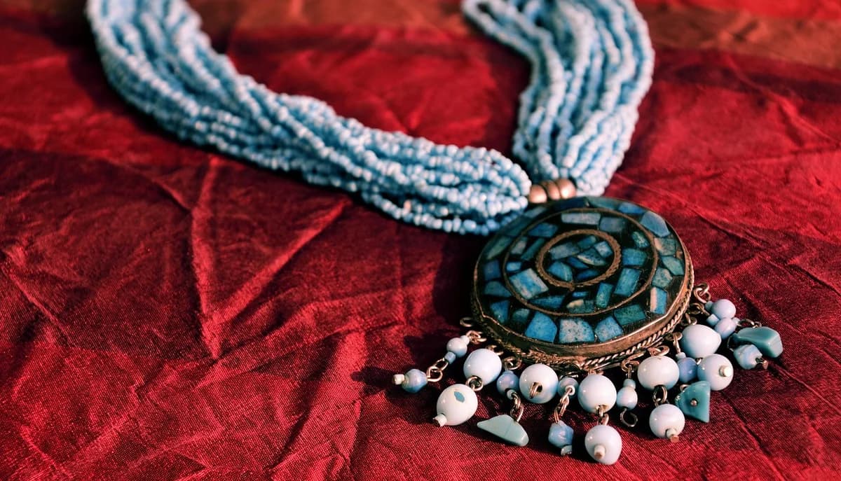 A decorative necklace with a circular blue pendant on red fabric.