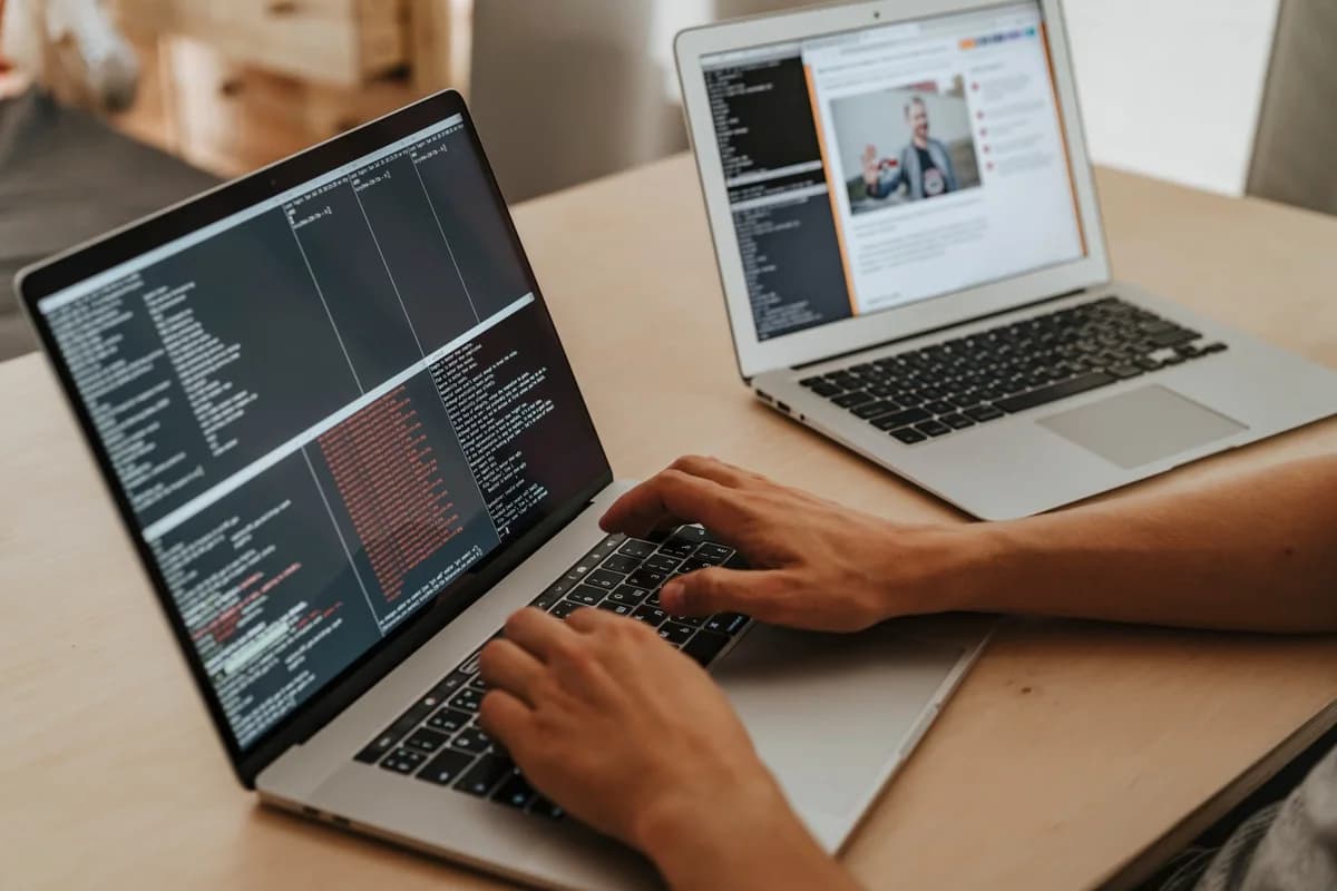 A person typing code on a laptop with another laptop nearby.