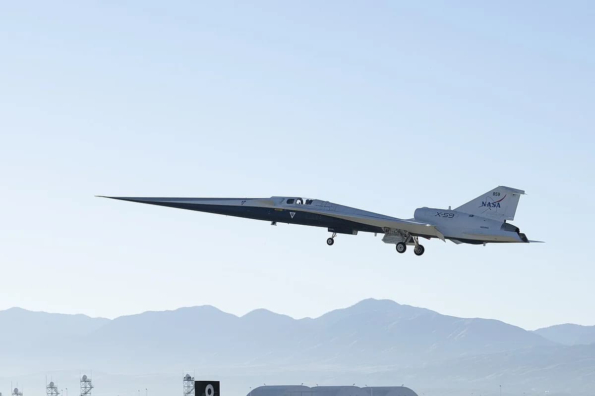 NASA X-59 research aircraft in flight over a desert landscape with mountains behind it.