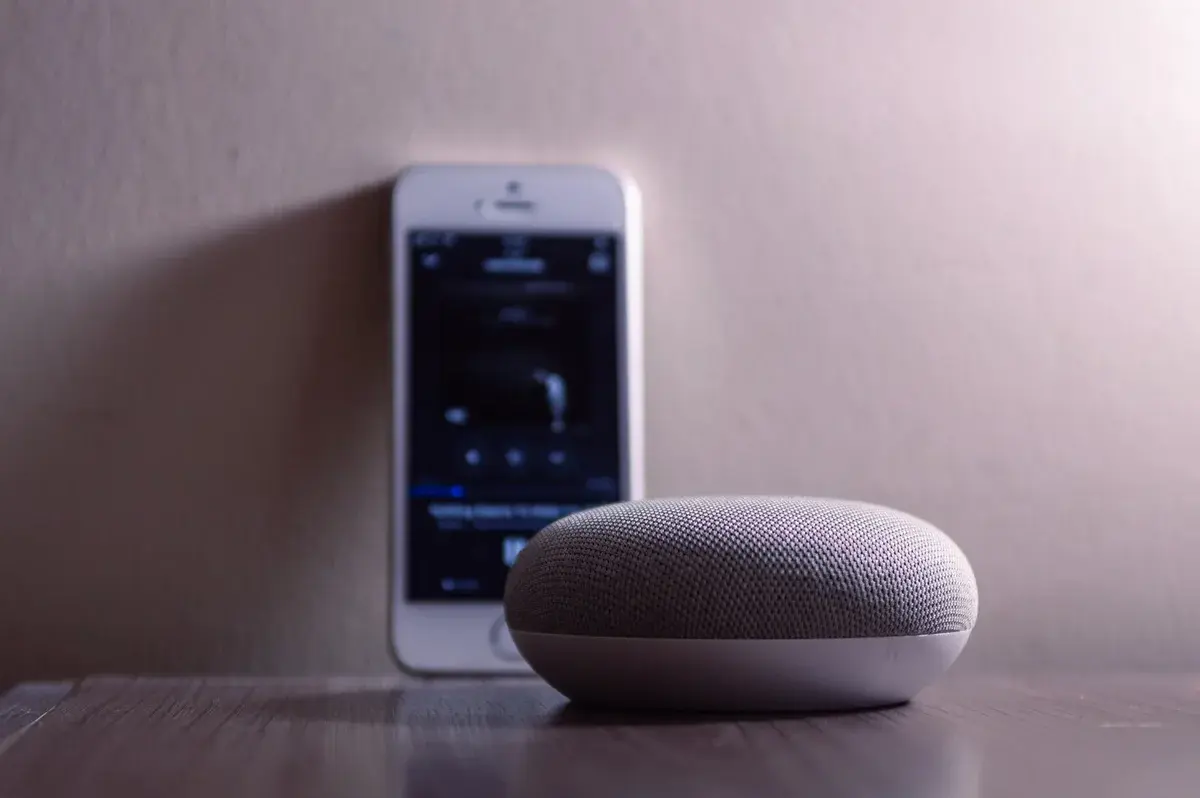 A smart speaker and a smartphone on a wooden table indoors.