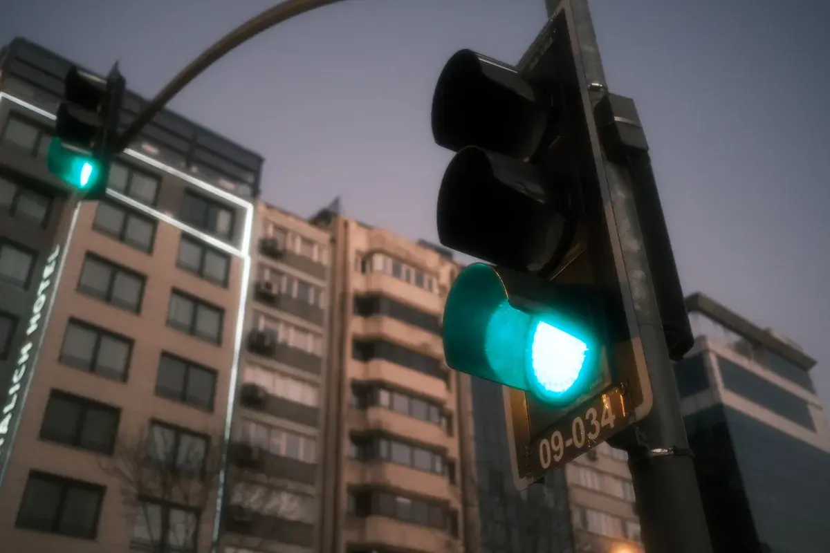 A green traffic light against city buildings at dusk.