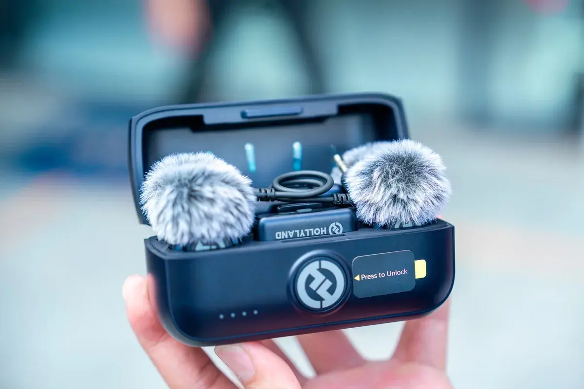A hand holding an open case with a compact dual microphone set inside.