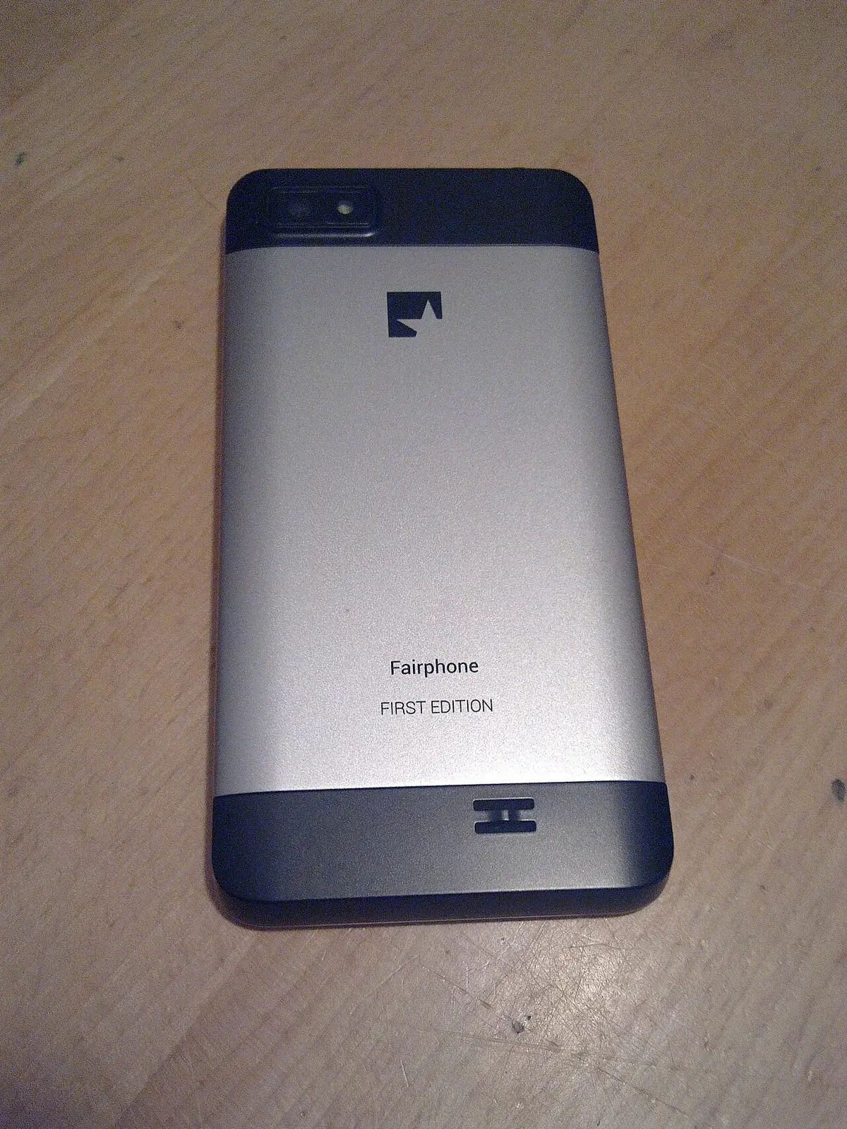 Back of a first-edition Fairphone smartphone on a wooden surface.