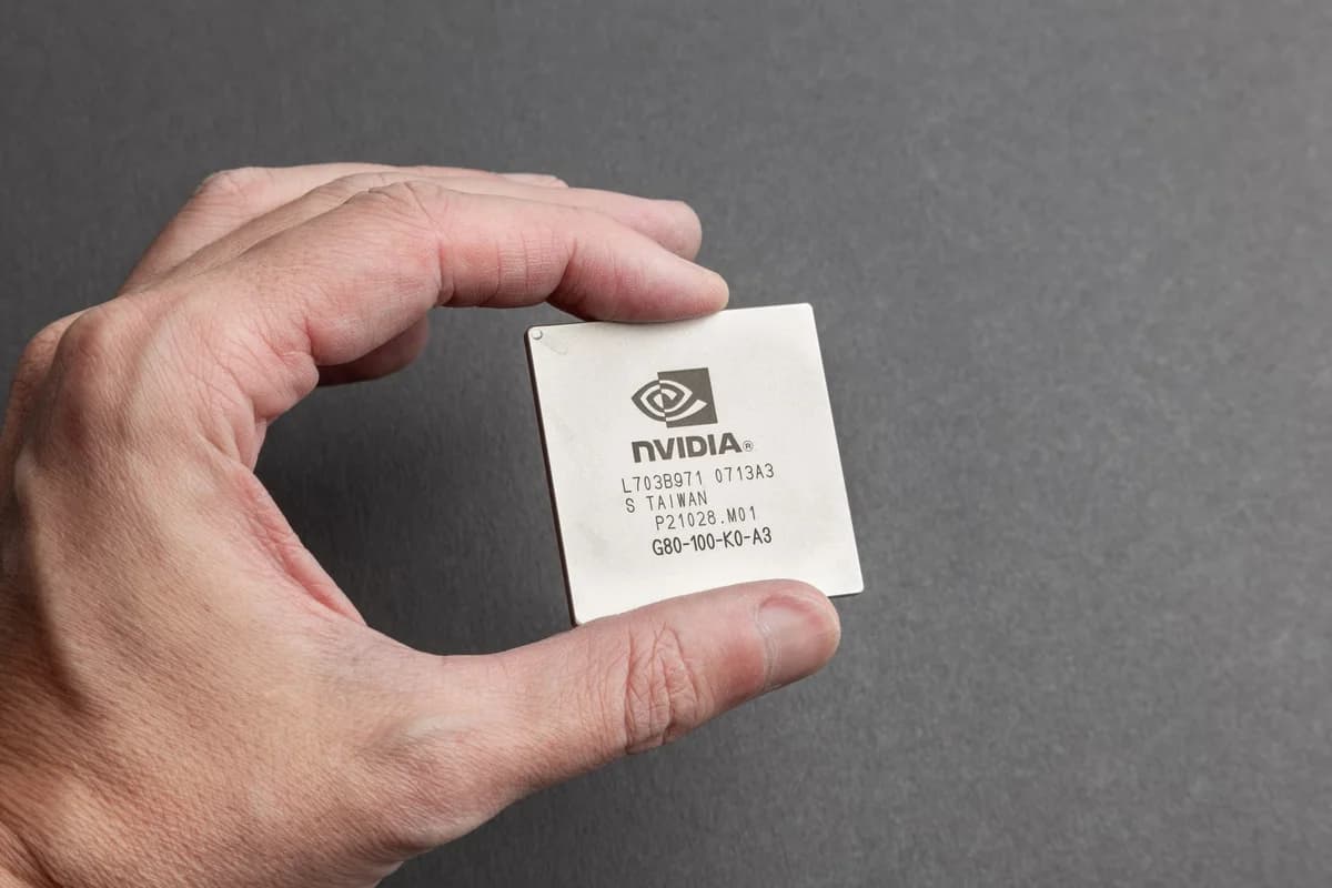A hand holding an Nvidia chip against a gray background.