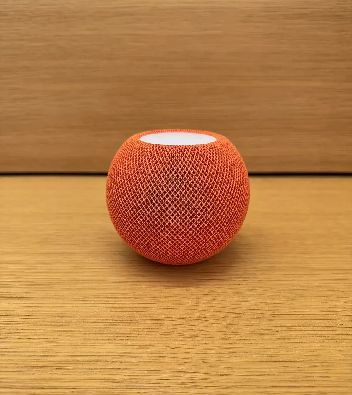 An orange Apple HomePod mini smart speaker on a wooden surface.