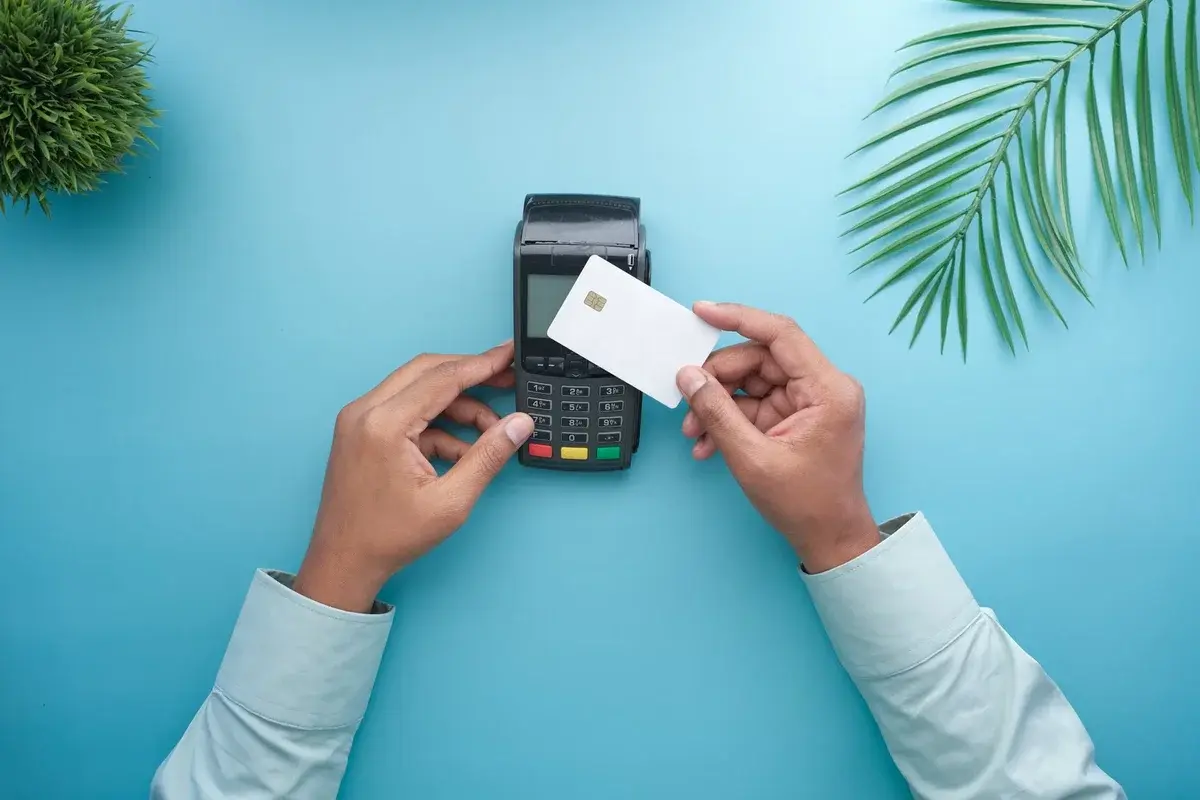 Hands holding a credit card near a payment terminal on a blue background.