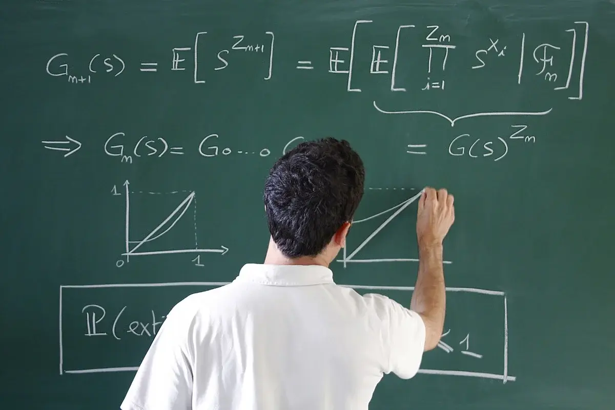 A person writing mathematical formulas on a chalkboard.