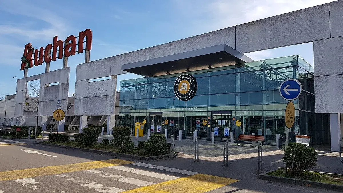 Exterior of an Auchan shopping center entrance with glass facade and signage.