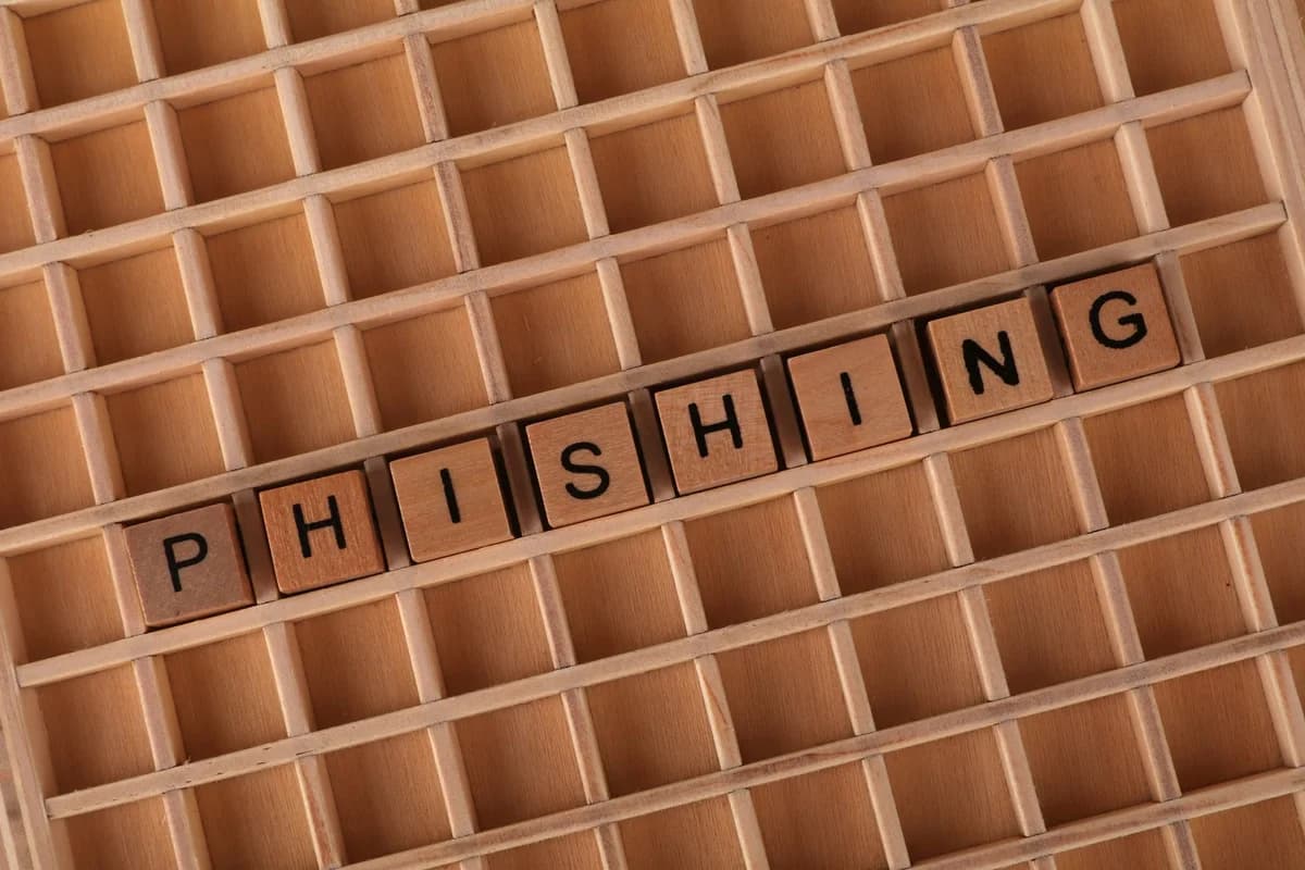 Wooden Scrabble tiles spelling 'PHISHING' in a tray.