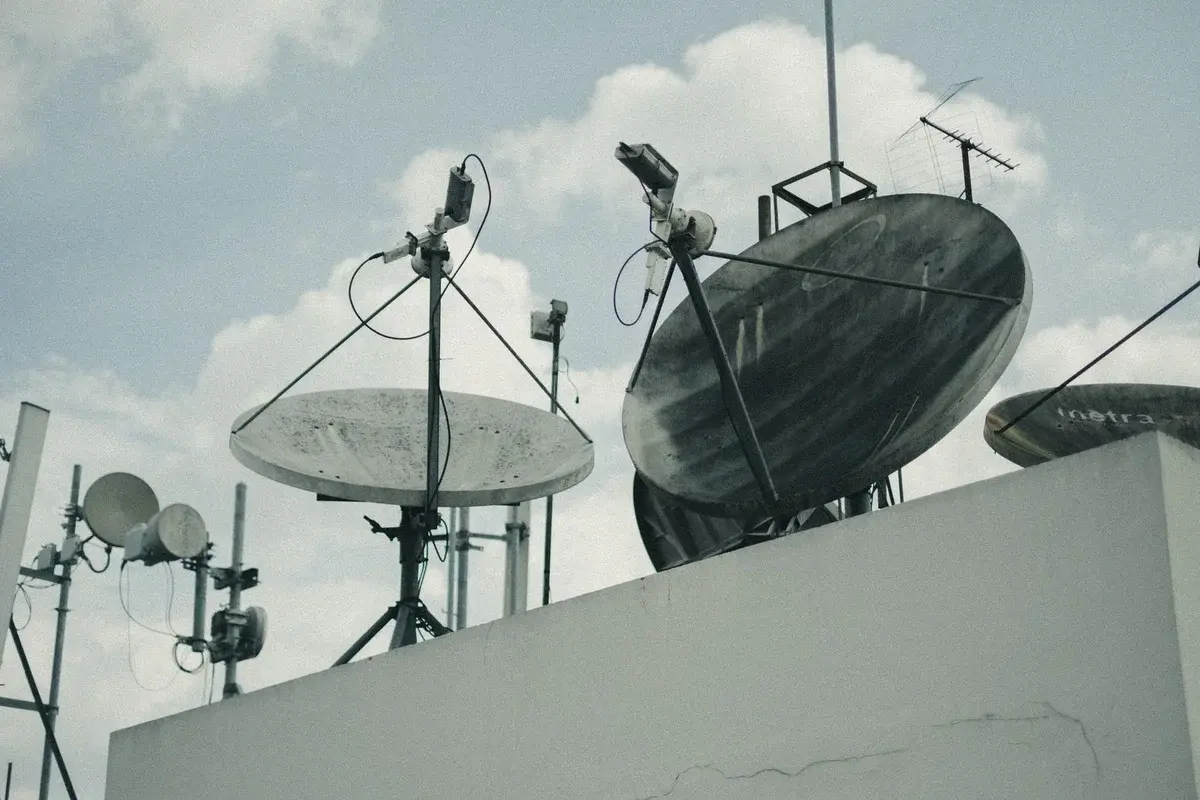Satellite dishes and antennas on a rooftop under cloudy skies.