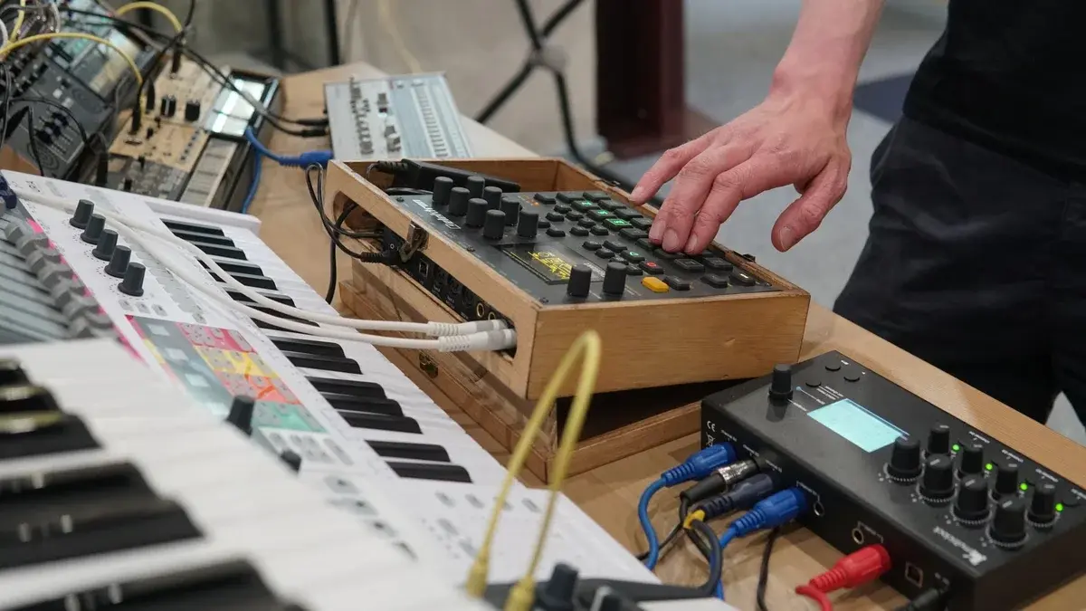 Hands adjusting electronic music equipment in a studio.
