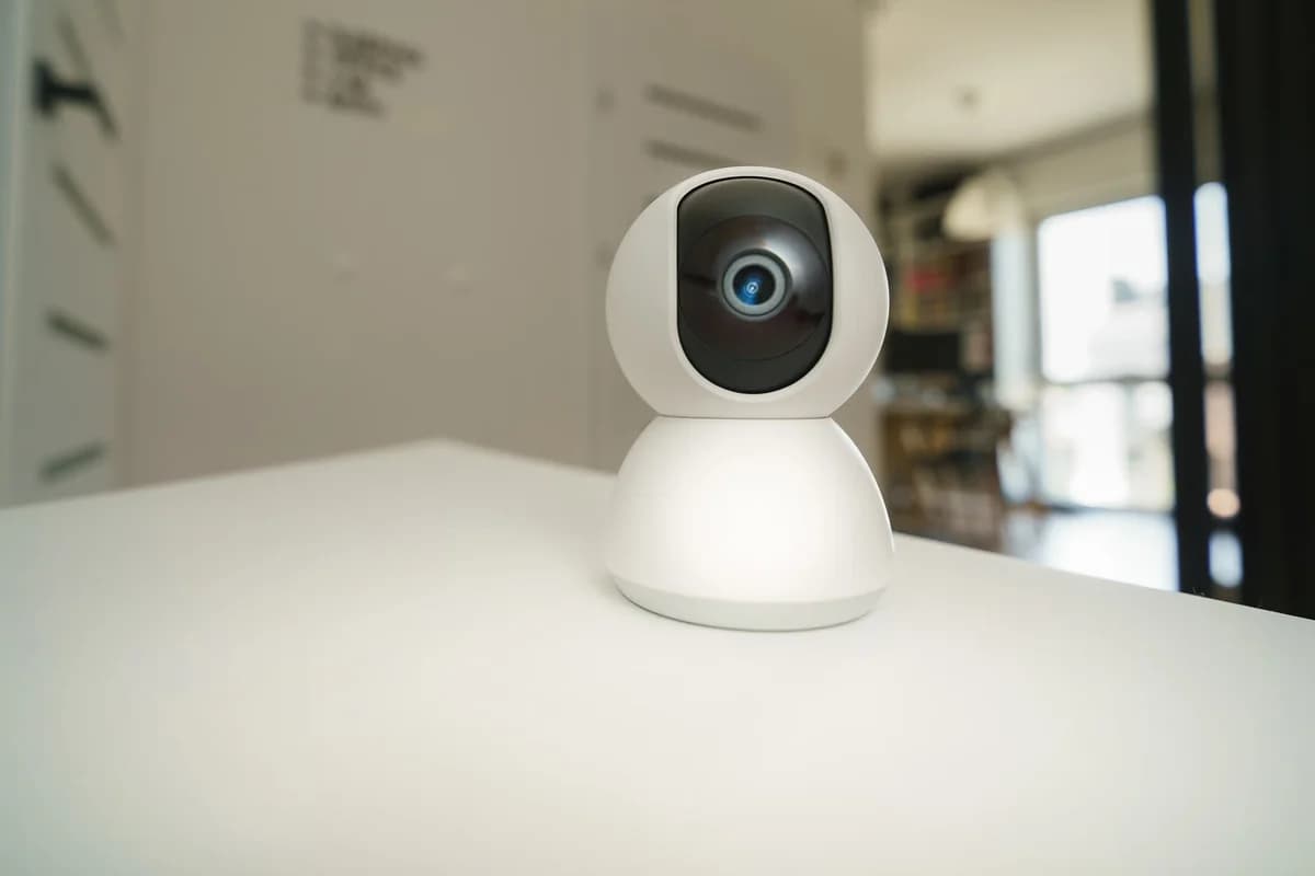 A white smart home security camera sitting on a table indoors.