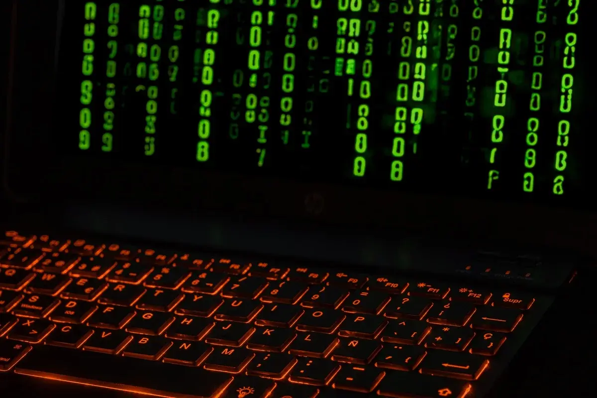 A laptop keyboard glowing orange with green digital code symbols above it.