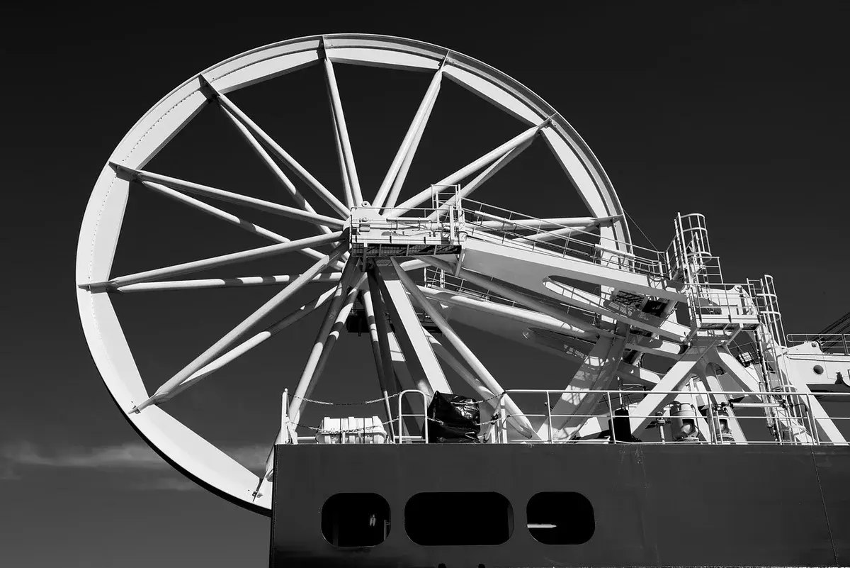 Black-and-white view of a submarine cable ship with a large cable-laying wheel.