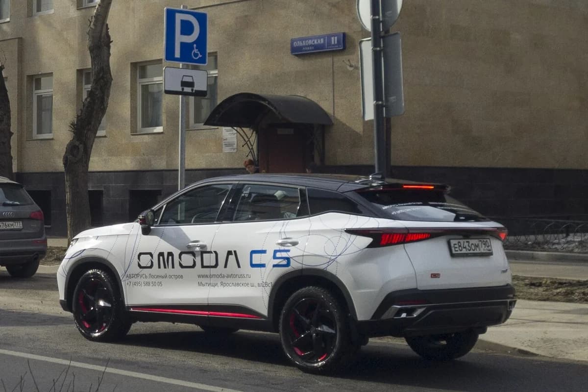 White Omoda C5 SUV parked on a Moscow street with dealership branding.