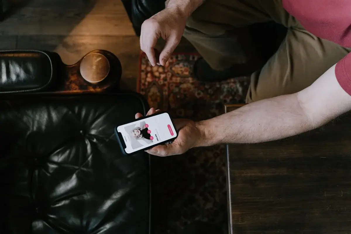 A person holds a smartphone showing a dating app while sitting in a leather chair.