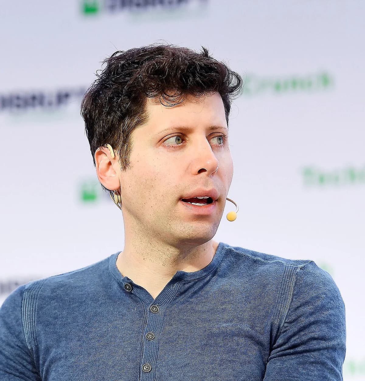 Sam Altman speaking on stage with a headset microphone.