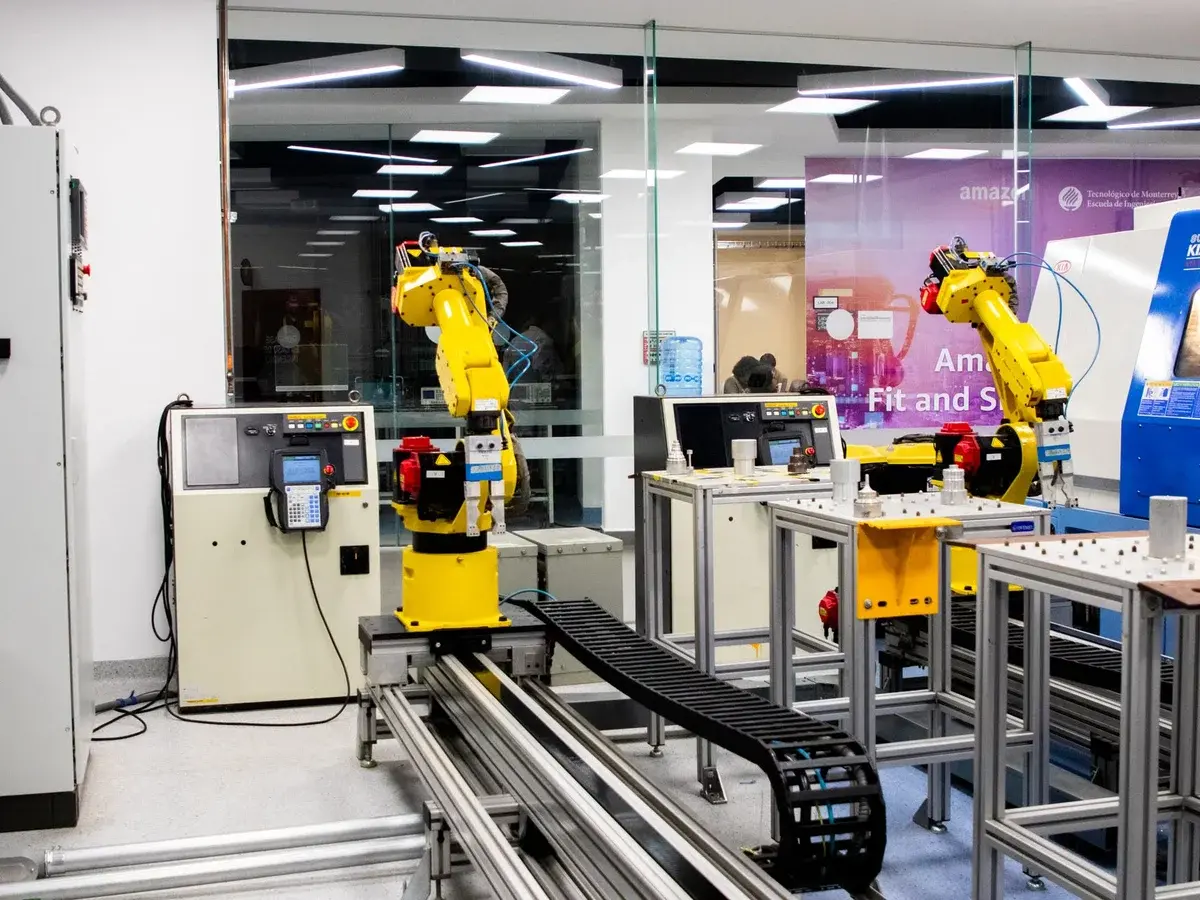 Two yellow industrial robotic arms in a modern lab with control panels and worktables.