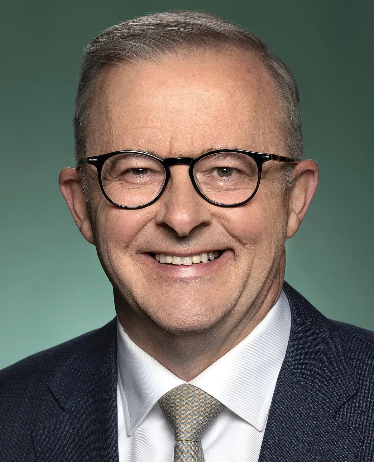 Official portrait of Australian Prime Minister Anthony Albanese smiling in a suit and glasses.