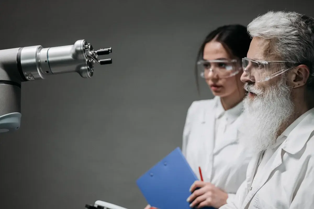 Two scientists in lab coats inspect a robot arm in a lab.