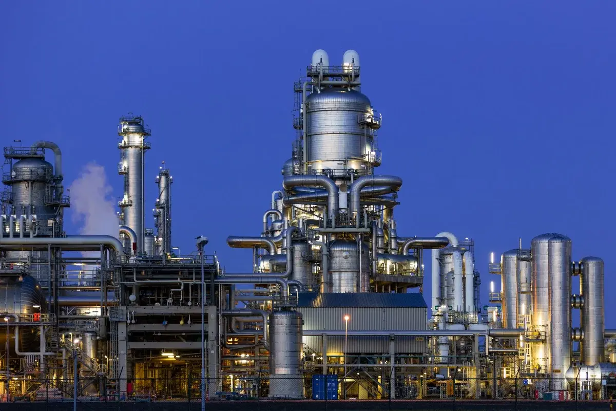 An illuminated oil refinery with steel towers and pipes at twilight.