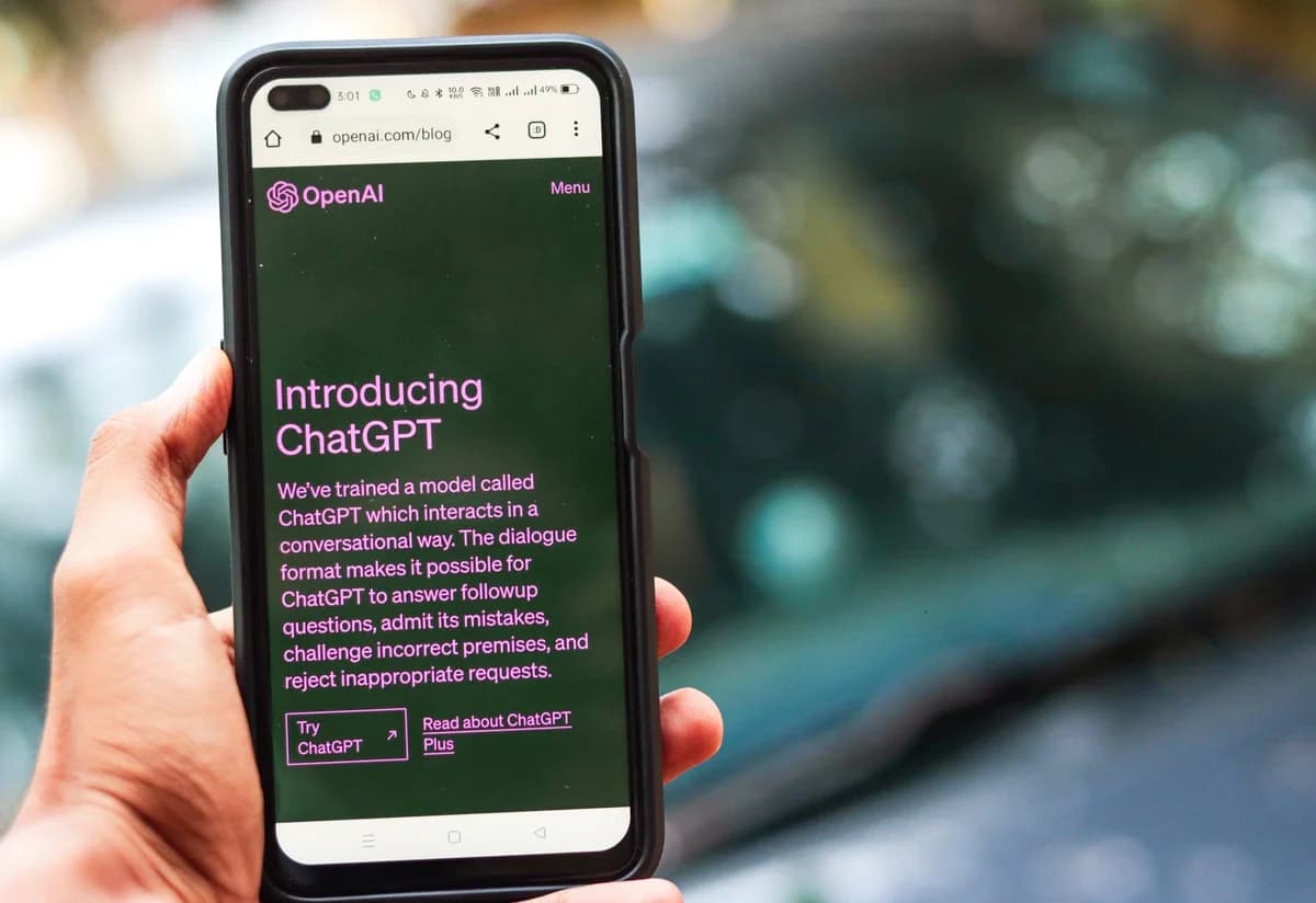 A hand holds a smartphone showing the OpenAI website with ChatGPT information.