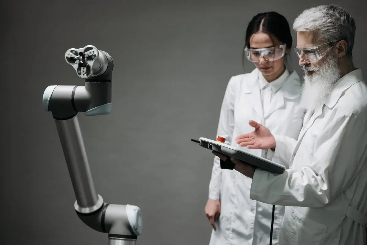 Two scientists in lab coats inspect a robot arm in a lab.