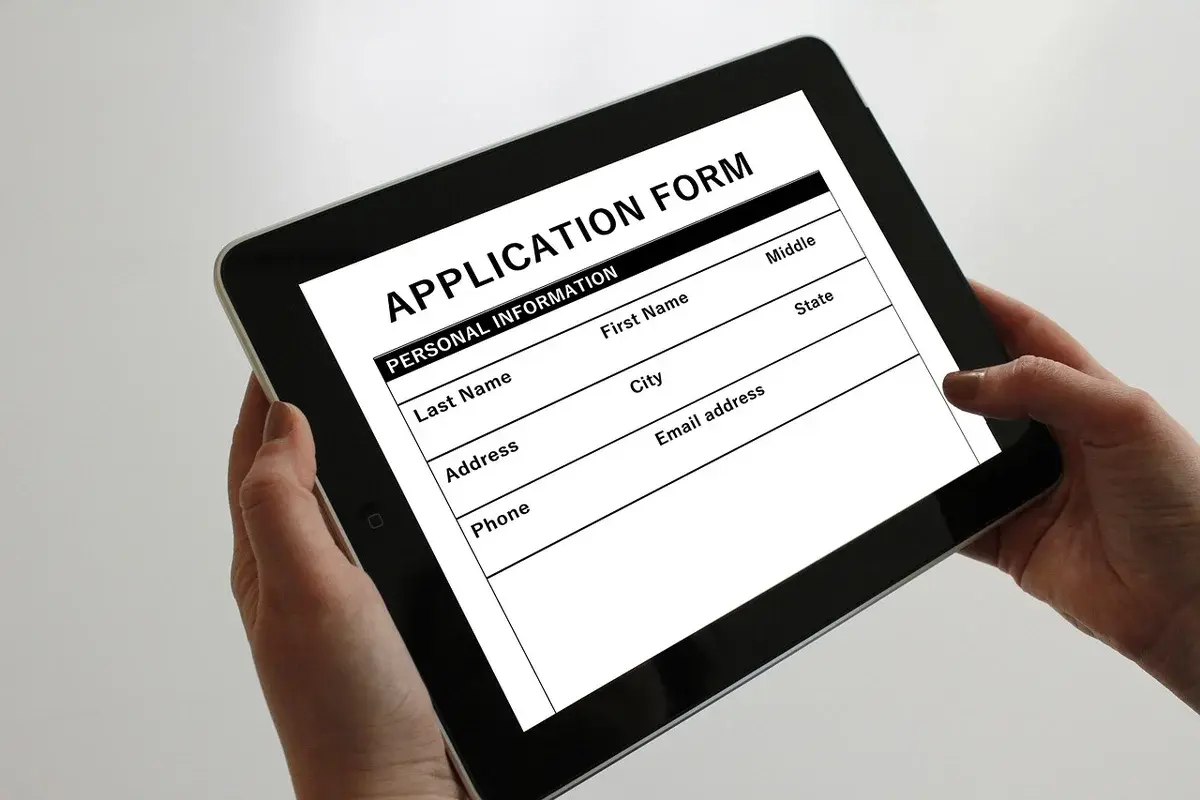 Hands holding a tablet showing an application form.