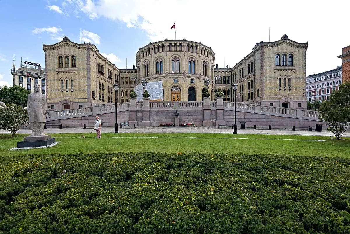 The Stortinget building in Oslo with a statue and a person walking a small dog in the foreground.